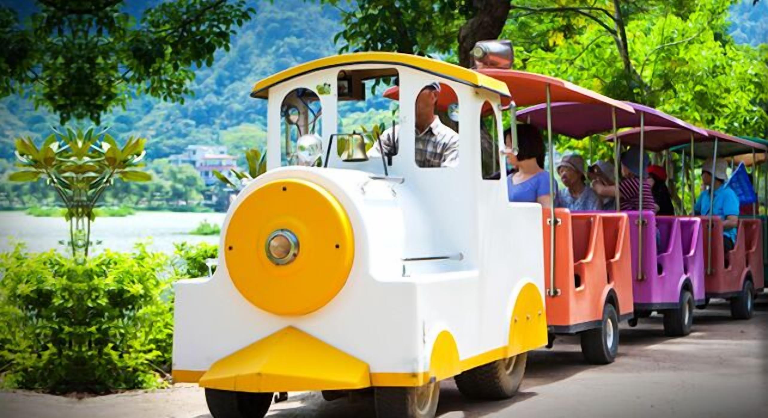 A small, colorful train with passengers, moving along a track surrounded by greenery.