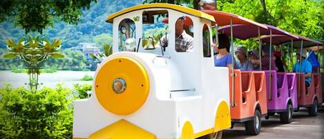 A small, colorful train with passengers, moving along a track surrounded by greenery.