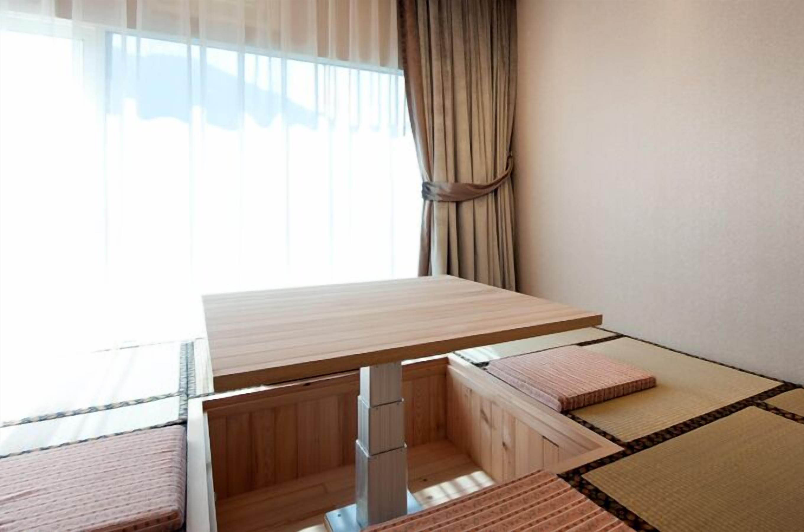 Una habitación con una mesa de madera, un banco, esteras de tatami y una ventana con cortinas.