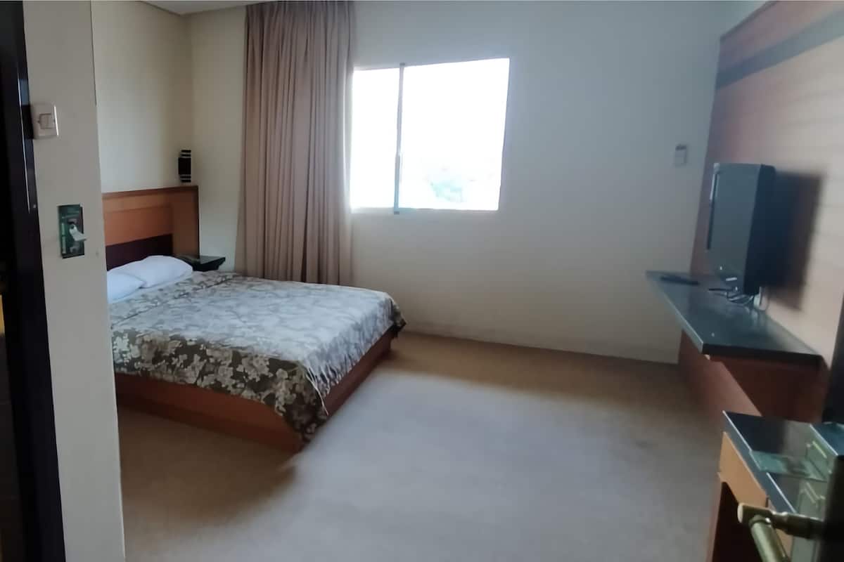 A hotel room with a bed, a desk, a TV, a window, and a curtain.