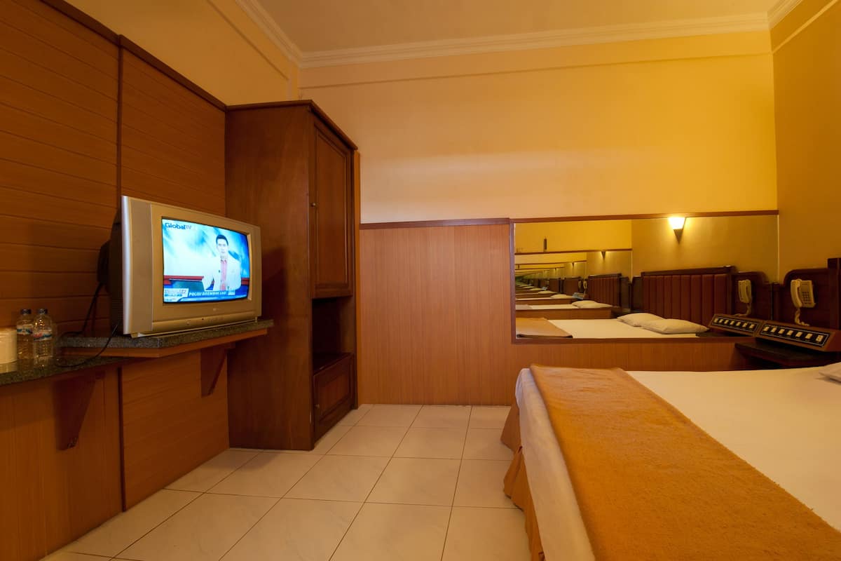 A hotel room with a bed, a TV, a mirror, and a bathroom visible in the background.