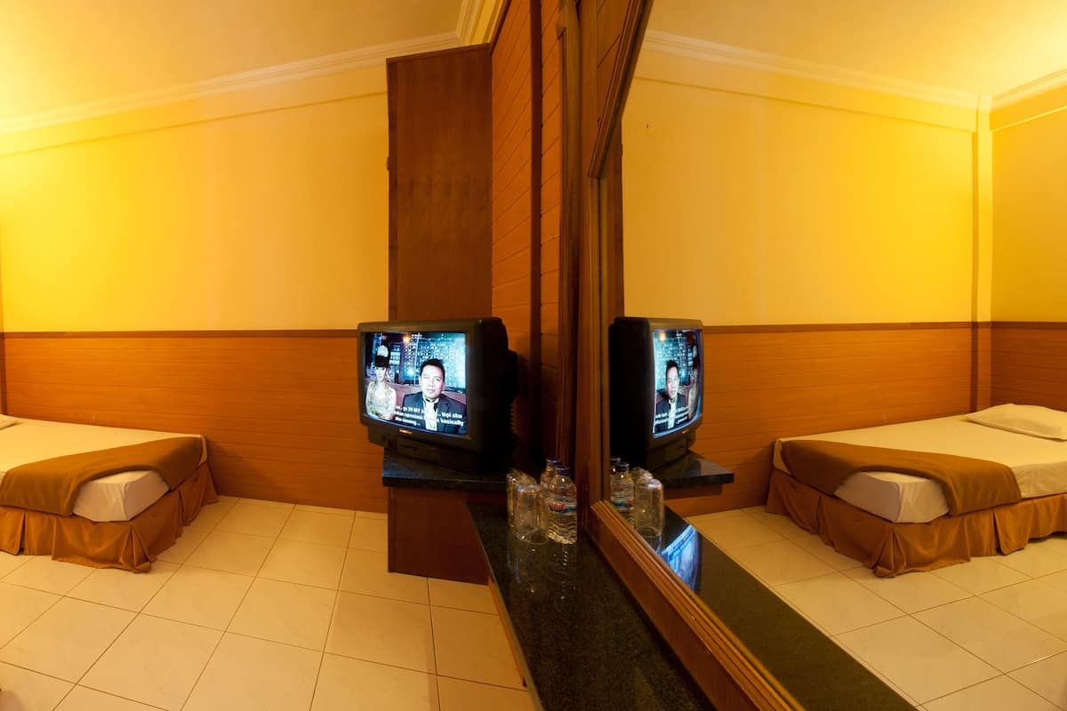 A hotel room with two single beds, a television on each side, a mirror, and a wooden headboard.