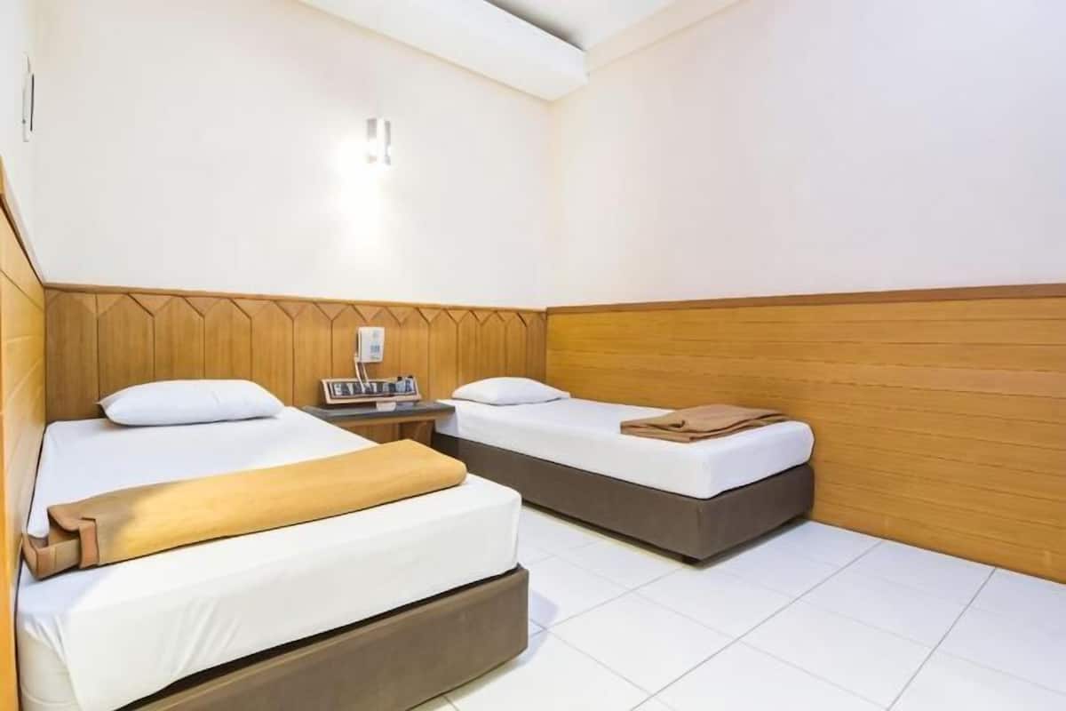 A hotel room with two beds, a wooden headboard, a nightstand, and a wall-mounted light.