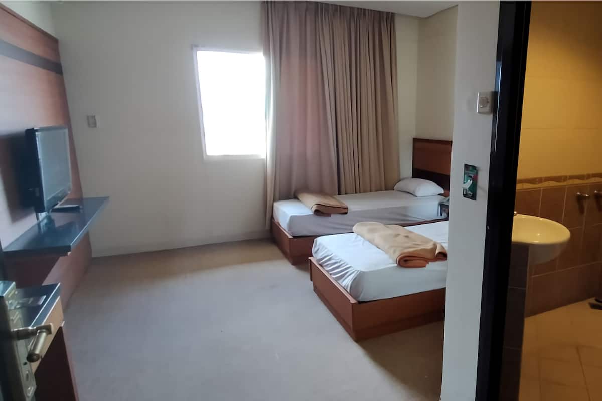 A hotel room with two beds, a TV, a window with curtains, and a bathroom with a sink.