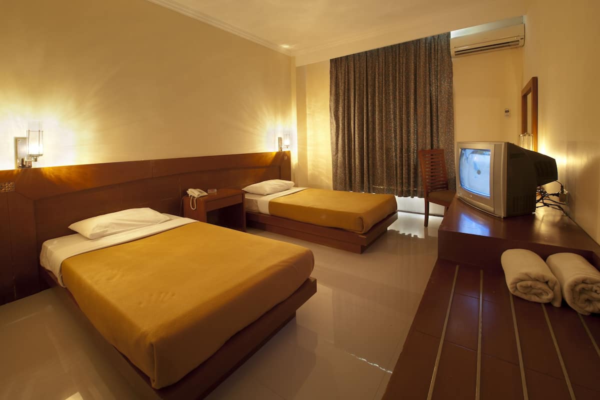 A hotel room with two beds, a television, a desk, and a window with curtains.