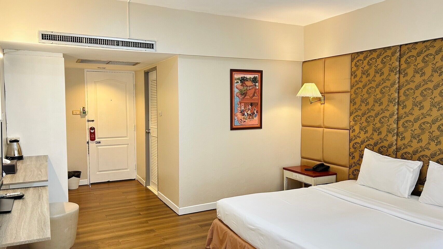 Een hotelkamer met een bed, nachtkastje, lamp en een deur naar een badkamer.