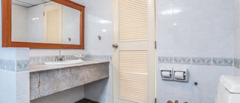 Un baño con lavamanos de mármol, espejo con marco de madera, inodoro con toalla y puerta con panel persiana.