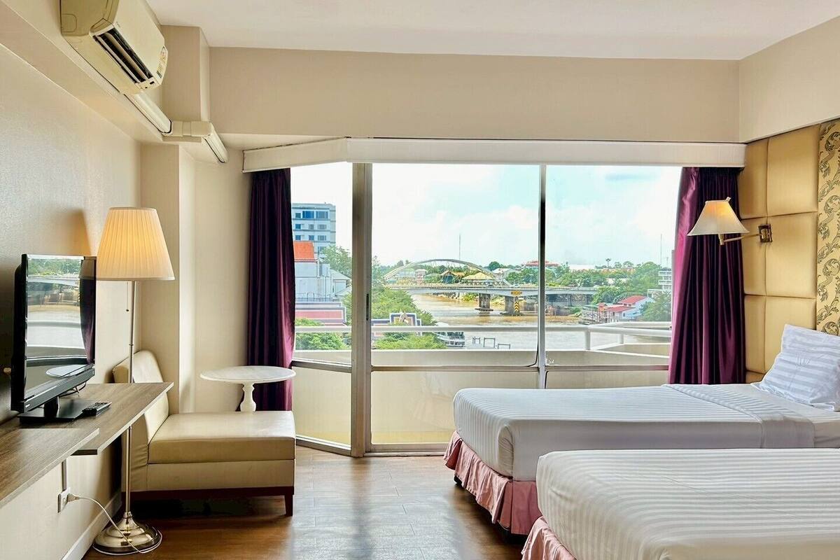 A hotel room with a bed, a desk, a chair, and a large window offering a city view.