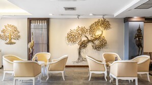 A reception area with a modern design, featuring a large wall art of a tree, white upholstered chairs, and a statue on the right. - Ayothaya Riverside Hotel Ayutthaya (Ayutthaya)