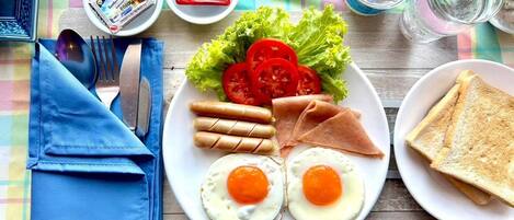 Un plato con huevos, salchichas, jamón y tomates sobre una mesa con mantel a cuadros.