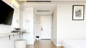 A modern hotel room with a bed, a desk with a flat-screen TV, a white chair, and a framed artwork on the wall. - Ayothaya Riverside Hotel Ayutthaya (Ayutthaya)