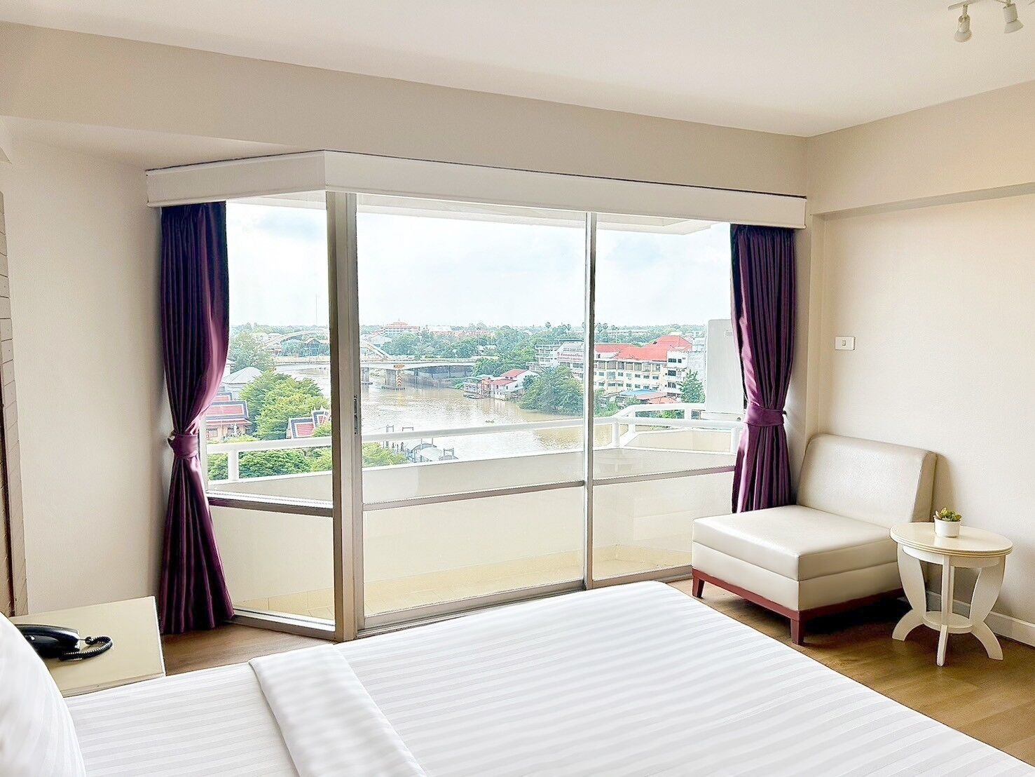 Habitación de hotel con un gran ventanal corredero, una cama, una silla y una mesita.