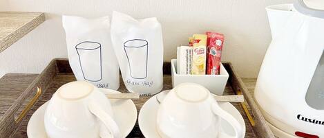 Una bandeja con dos tazas y platillos blancos, dos bolsas blancas con la etiqueta 'Glass Bag', una cafetera blanca y un recipiente blanco con sobres de café.