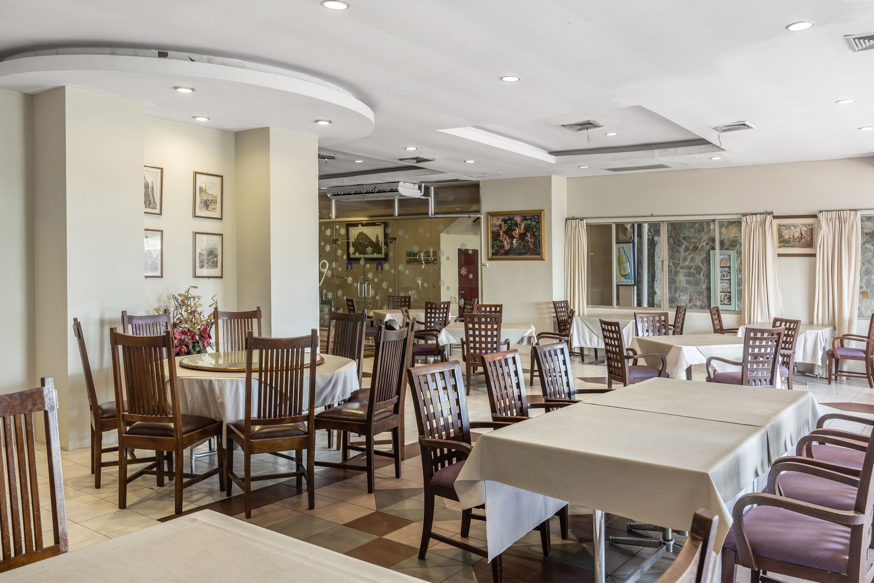 A dining area with multiple tables and chairs, a large painting on the wall, and framed pictures on the walls.