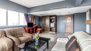 A modern living room with a sofa, a coffee table with a vase, and a television. There is a wardrobe and a door in the background. - Ayothaya Riverside Hotel Ayutthaya (Ayutthaya)
