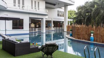 A pool area with a lounge chair and a table, a wooden fence, and a building with large windows and a balcony.