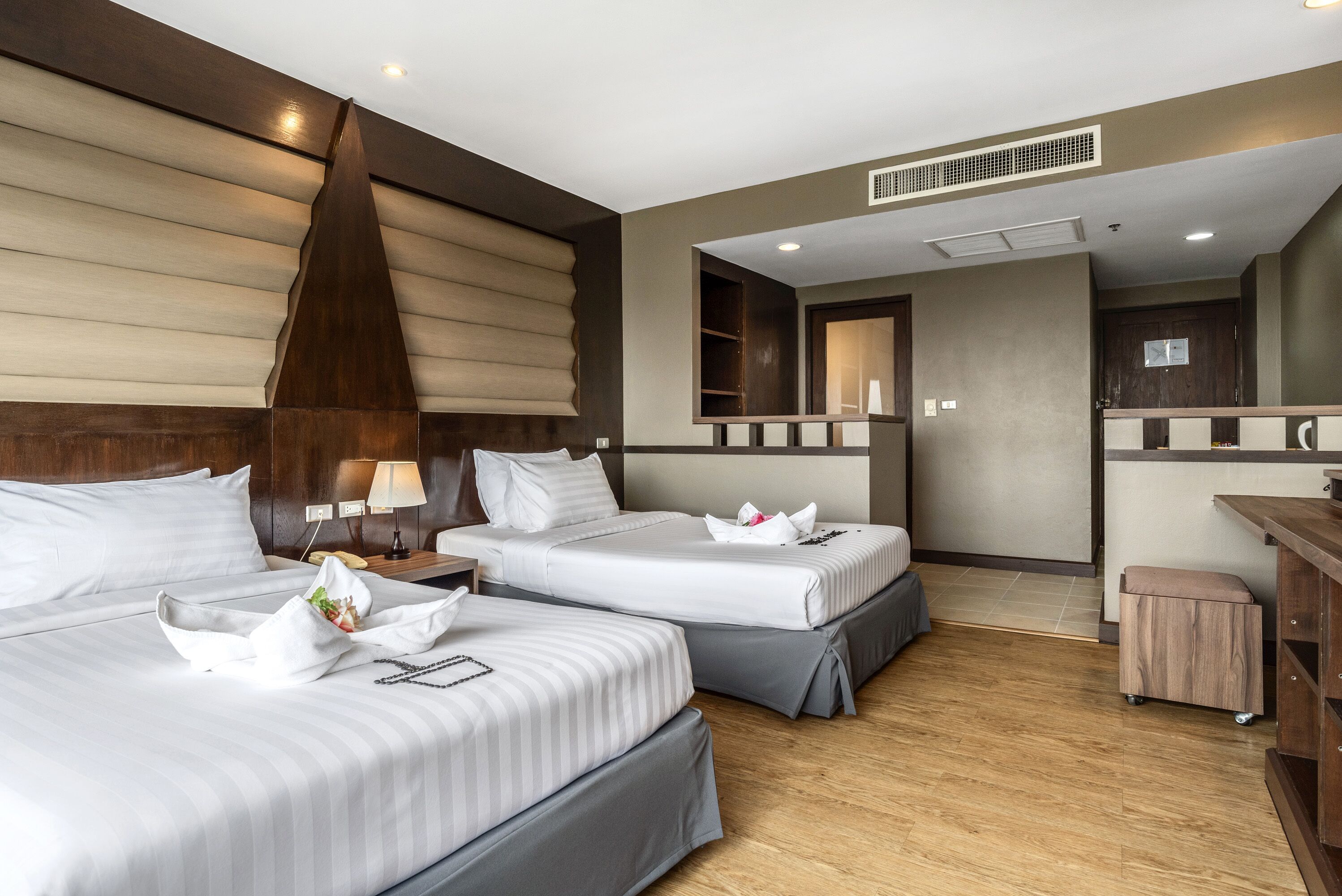 A hotel room with two beds, a wooden headboard, a small desk, and a mirror.