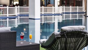 Ein Poolbereich mit Korbstühlen und einem Glas rotem Getränk.