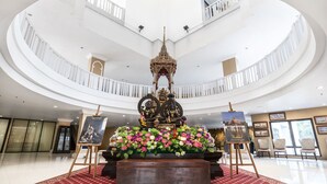 Ein mehrgeschossiges Atrium mit einer zentralen Buddha-Statue, umgeben von floralen Dekorationen und Kunstwerken.