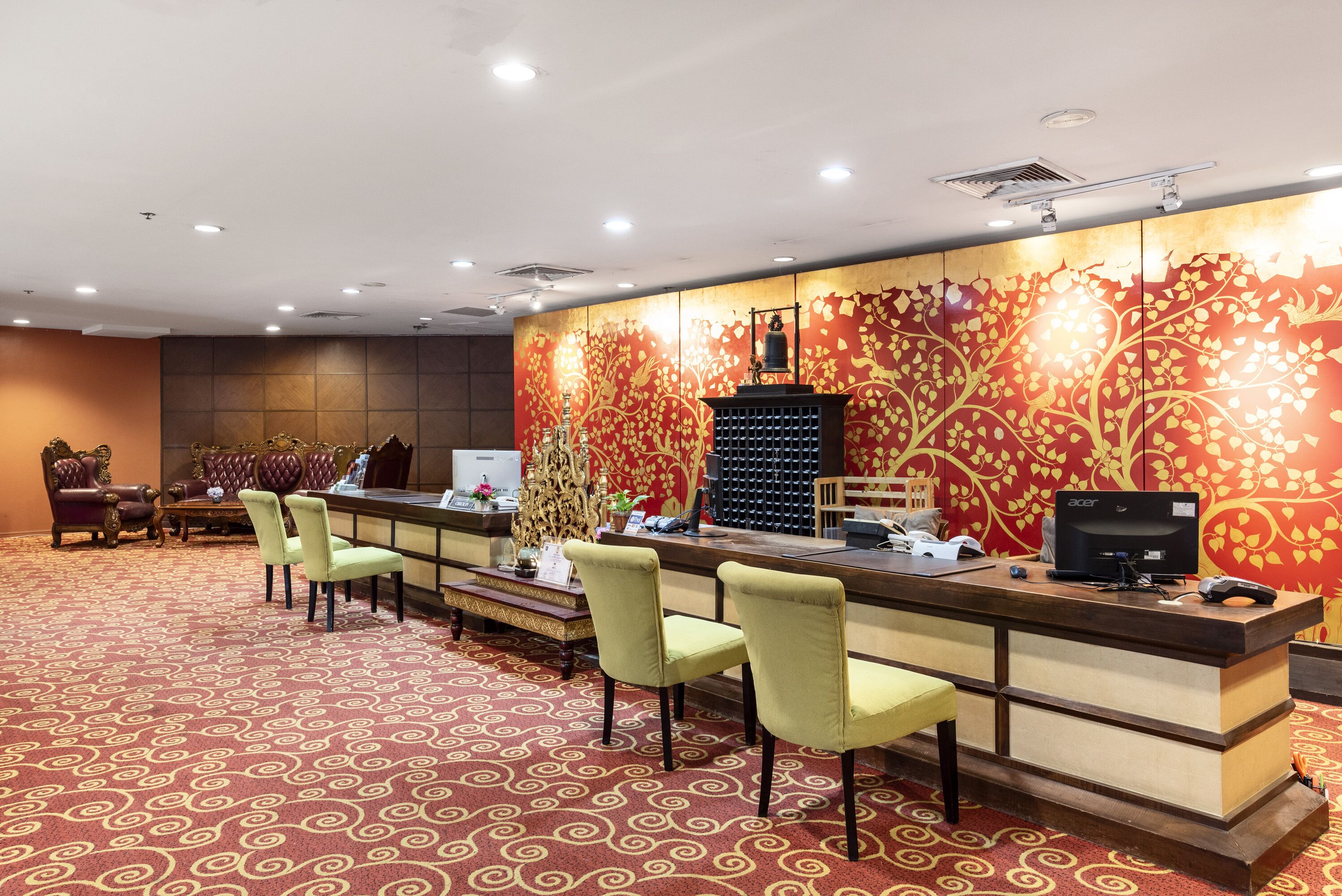 Ein Hotel-Empfangsbereich mit einem gemusterten Teppich, einem Empfangstresen, Stühlen und einer Wandverzierung.