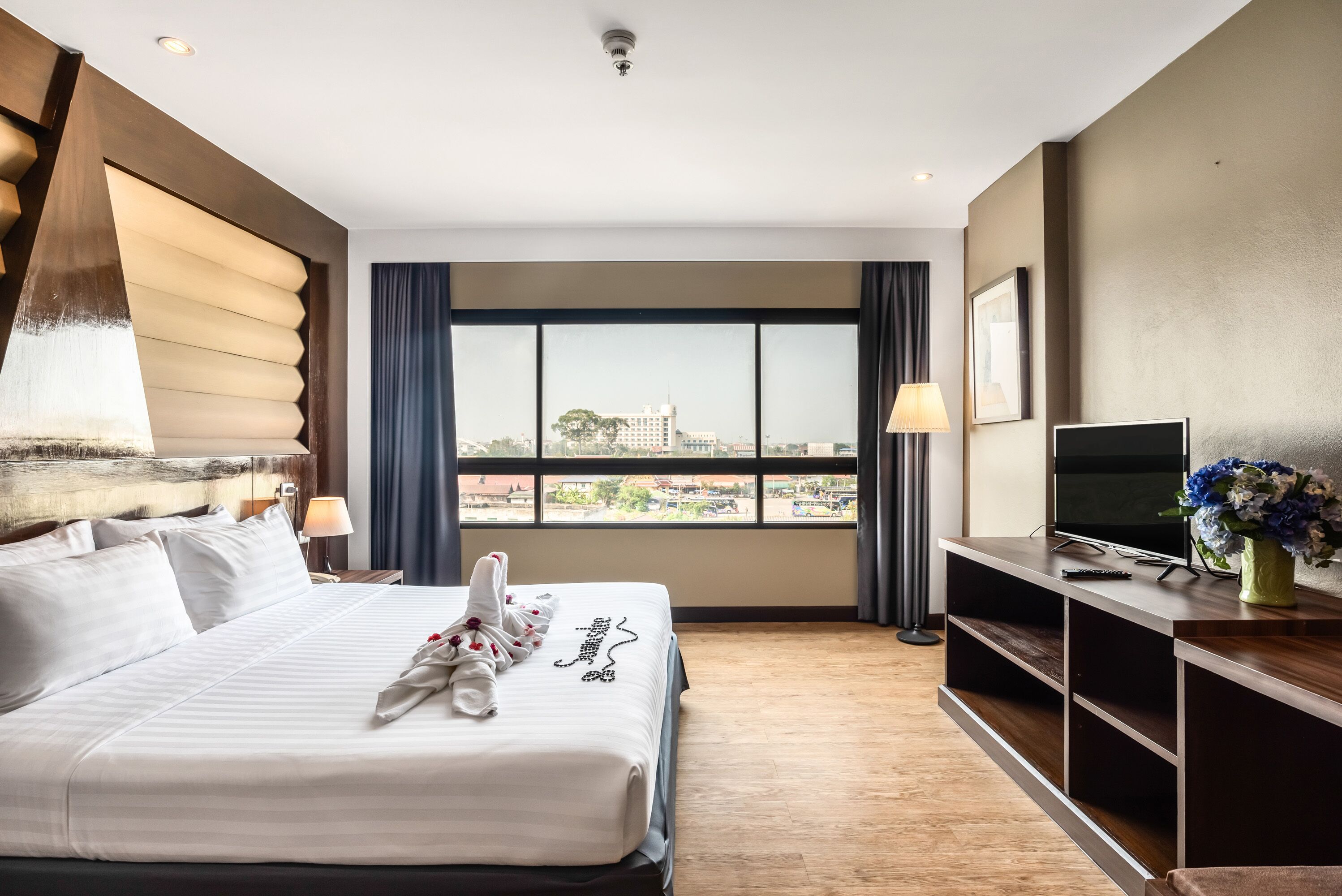 A hotel room with a large bed, a TV, and a view of the city.