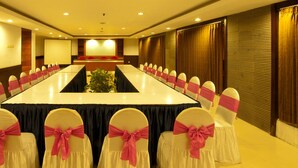 Une salle de conférence avec une longue table, des chaises ornées de rubans roses et un écran de projection.