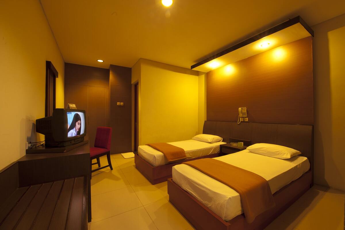A hotel room with two single beds, a TV on a small table, and a red chair.