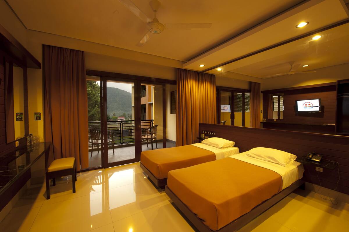 A hotel room with two beds, a TV, a desk, and a balcony with a view of the mountains.