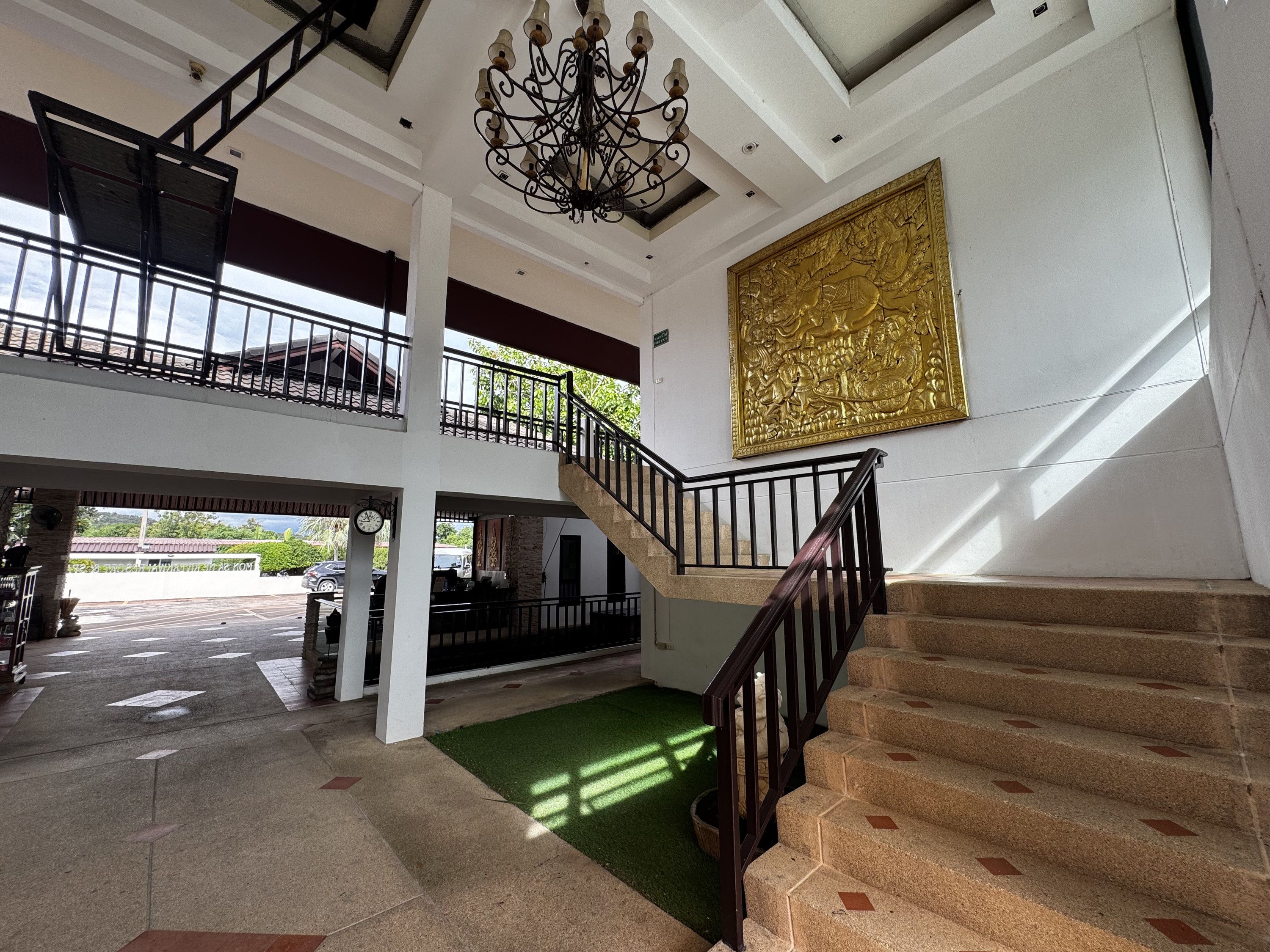 A multi-level interior with a staircase, a chandelier, and a large golden artwork.