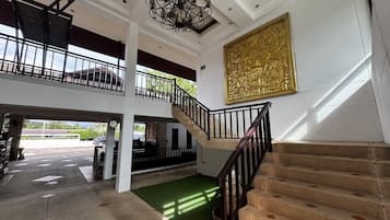 A multi-level interior with a staircase, a chandelier, and a large golden artwork.