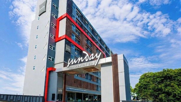 Un hotel moderno con un llamativo letrero que dice 'Sunday', una construcción de varios pisos y un cielo despejado.