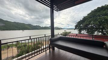 Varanda com vista para um lago e montanhas, com guarda-corpo vermelho e um banco preto.