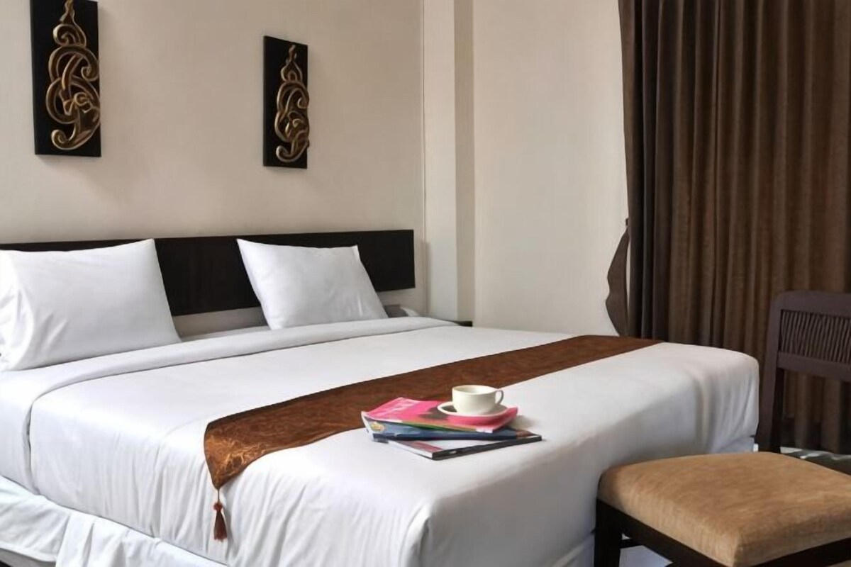 A hotel room with a bed, a bedside table, a chair, and a window with curtains.