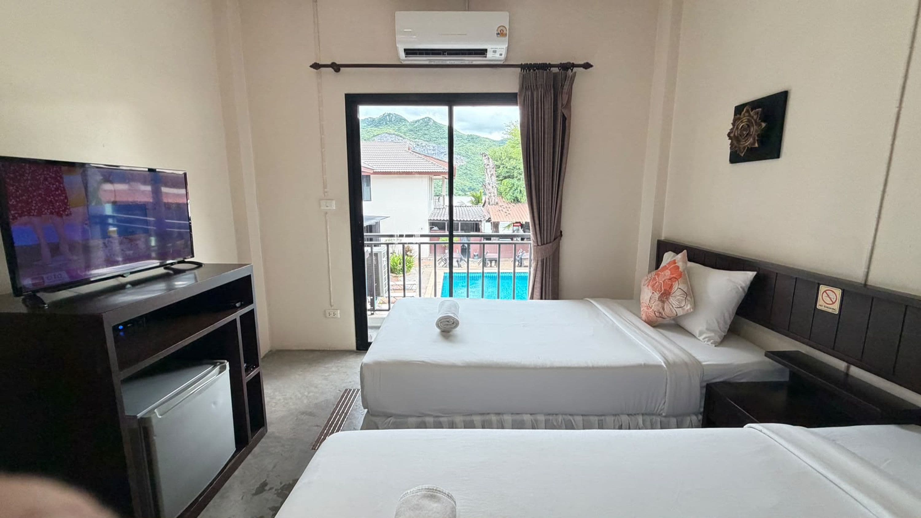 A hotel room with two beds, a television, a small refrigerator, and a balcony with a pool view.