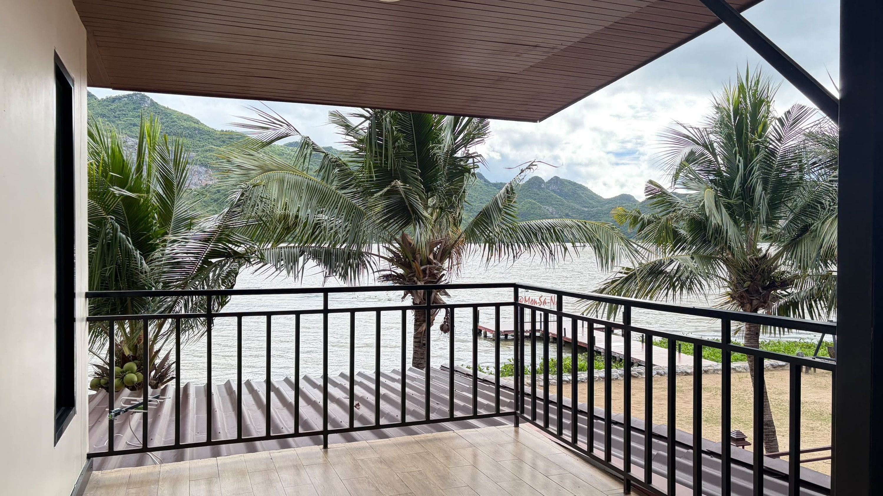 A balcony with a view of a lake and mountains, featuring palm trees and a metal railing.