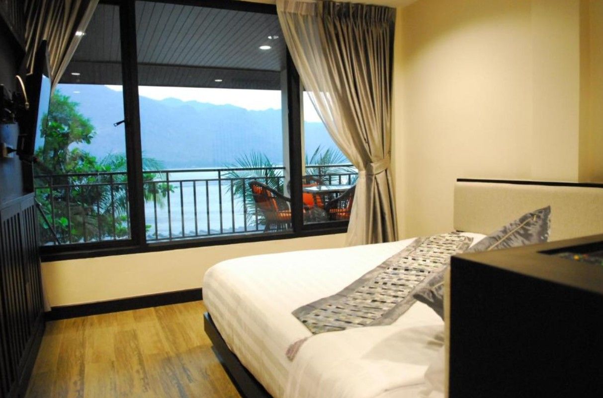 A hotel room with a bed, a TV, and a view of the sea and mountains through large windows.