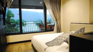 A hotel room with a bed, a TV, and a view of the sea and mountains through large windows.