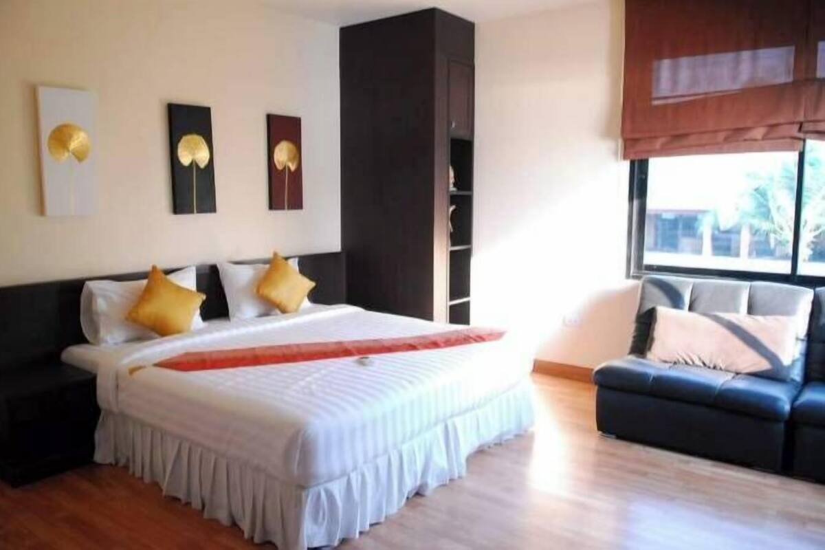 Une chambre d’hôtel moderne avec un grand lit, un canapé de couleur sombre et une fenêtre donnant sur un beau paysage.