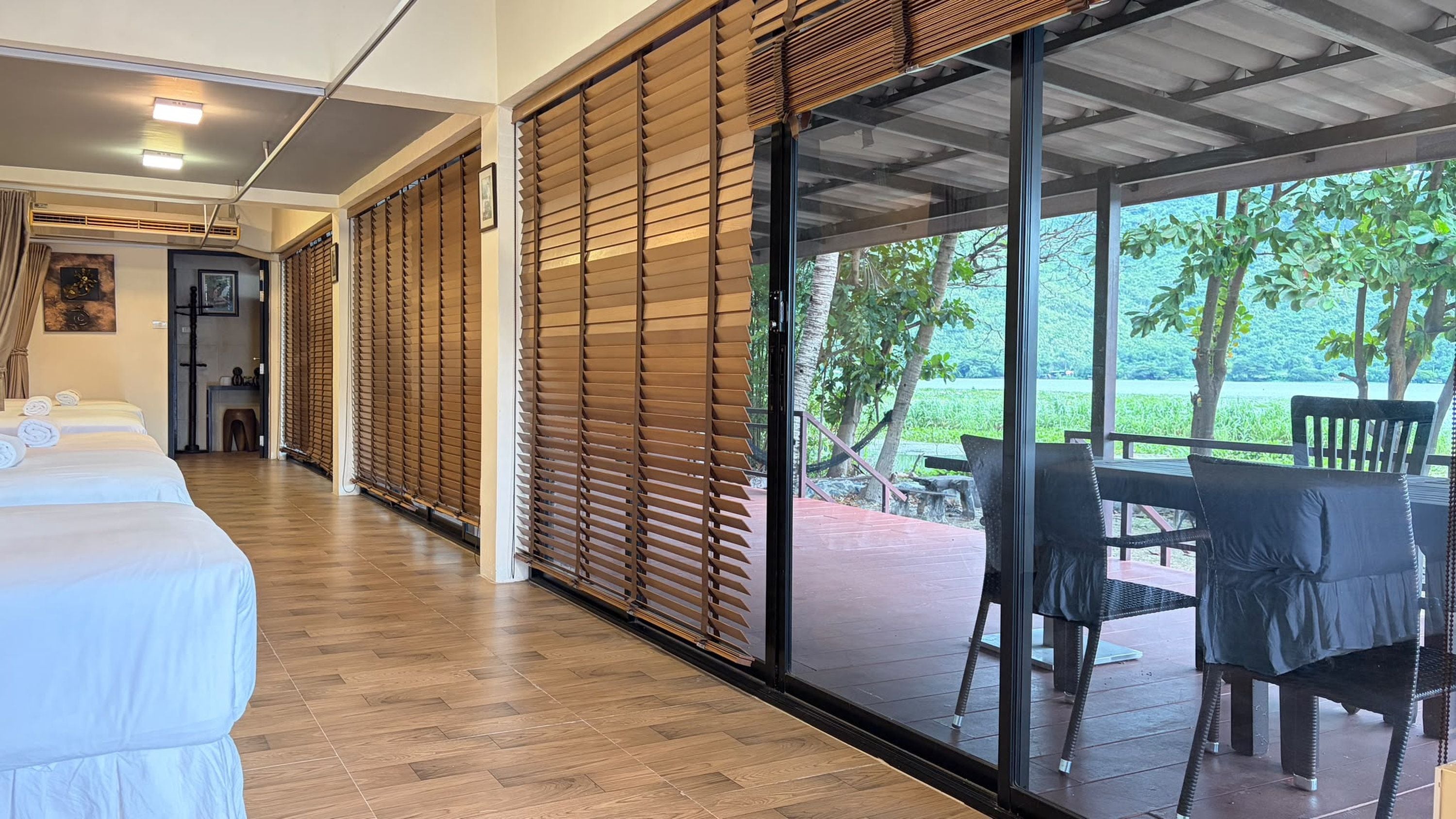 A hotel room with a wooden floor, a bed with white linens, a sliding glass door leading to an outdoor area with a table and chairs.