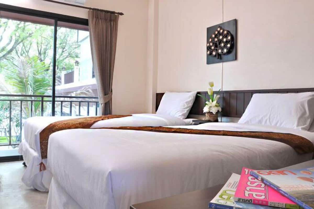 Une chambre d’hôtel avec deux lits, un balcon donnant sur la verdure et un luminaire fixé au mur.