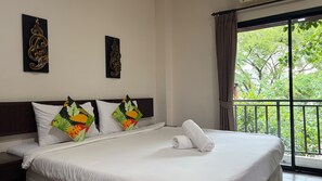 A hotel room with a bed, pillows, a window with a view of greenery, and wall art.