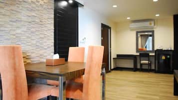 A dining area with a wooden table and four chairs, a stone wall, and a small kitchen area with a refrigerator and a sink.