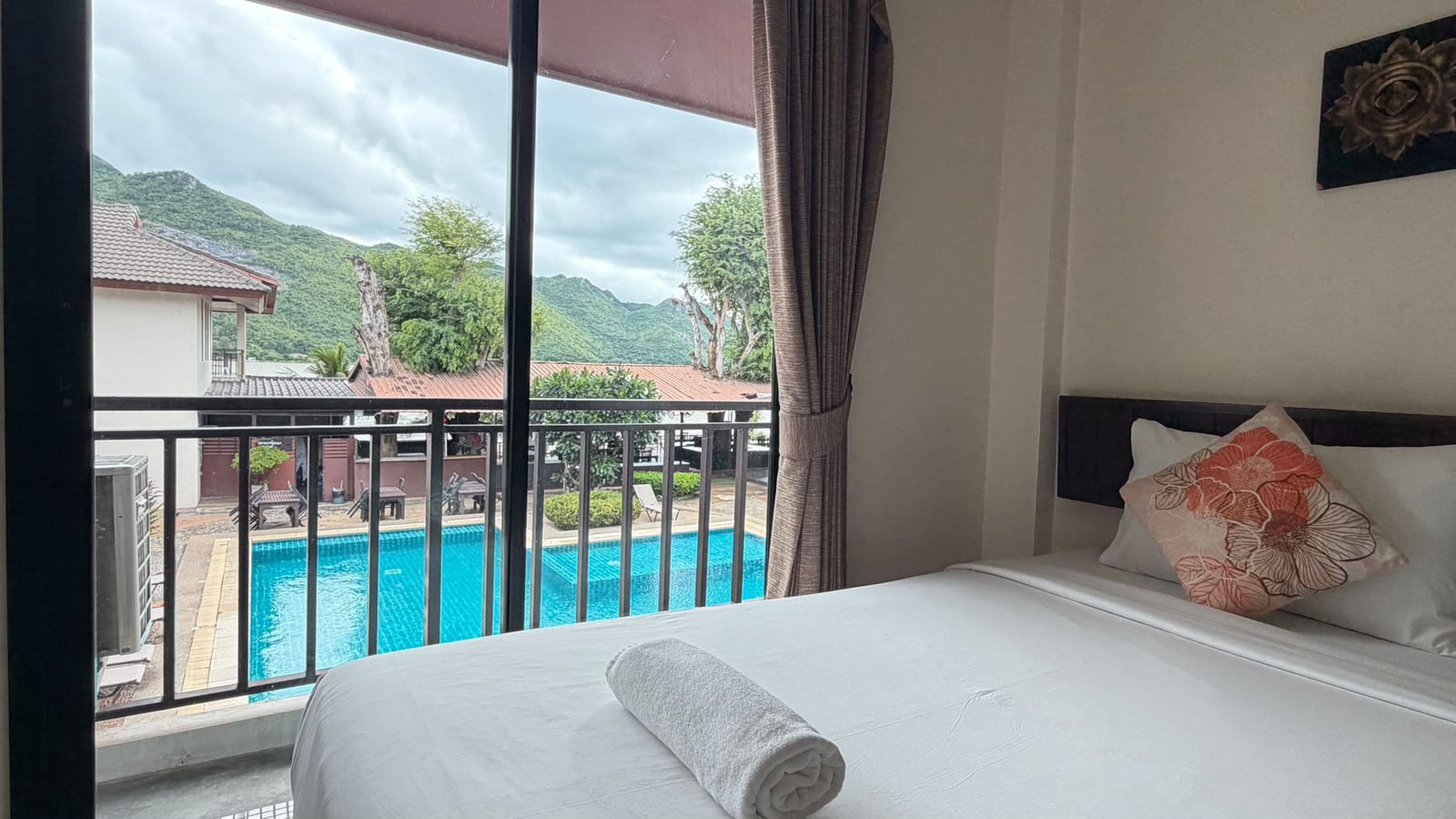 Een hotelkamer met een bed, uitzicht op een zwembad en een balkon.