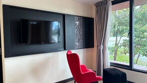 A modern room with a flat-screen TV mounted on the wall, a red chair, and a window with curtains. - Palette Monsane River Kwai Resort (Kanchanaburi)