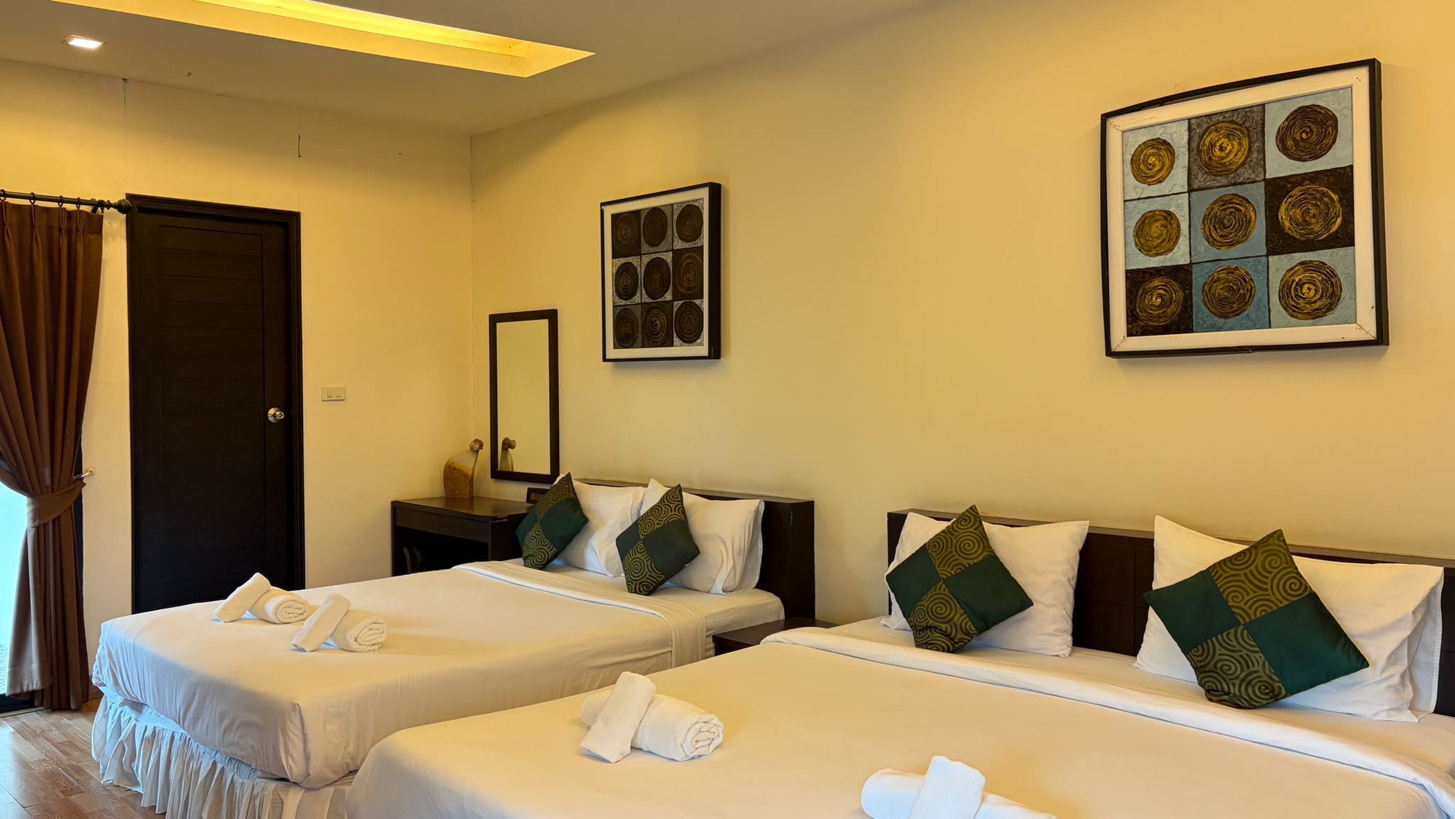 A hotel room with two beds, a desk, a mirror, and artwork on the walls.