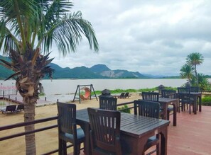 An outdoor seating area with tables and chairs, overlooking a body of water and mountains. - Palette Monsane River Kwai Resort (Kanchanaburi)