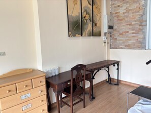 A room with a wooden dresser, a desk with a chair, a painting on the wall, and a brick-patterned wall.
