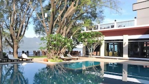 Piscina com espreguiçadeiras, um edifício com grandes janelas e vista para o mar.