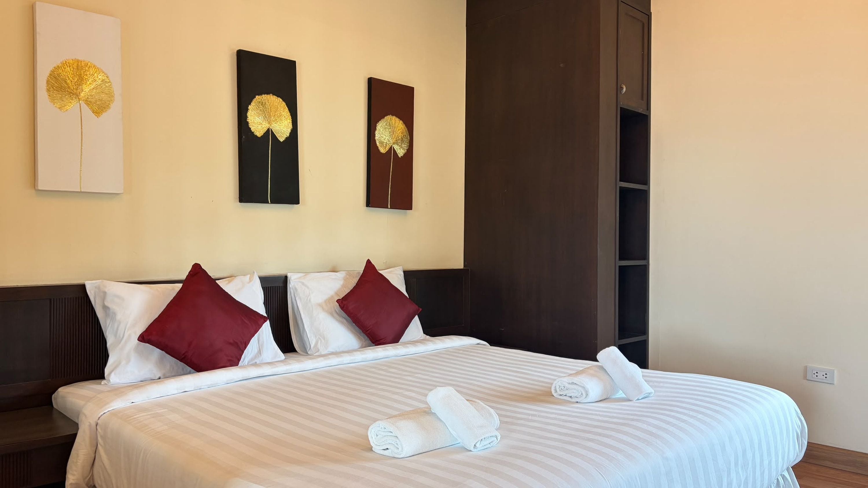 A hotel room with a large bed, two pillows, a headboard, and three wall-mounted artworks.