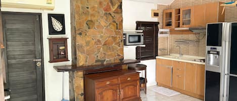 A kitchen with a stone wall, wooden cabinets, a microwave, and a refrigerator.